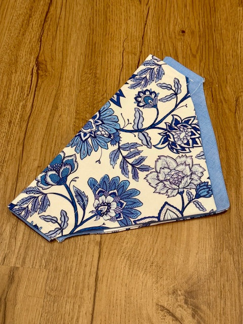 A blue and white floral boho dog bandana laid out on a wooden surface.