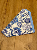 A blue and white floral boho dog bandana laid out on a wooden surface.