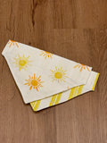 Bright yellow reversible dog bandana with sun print and yellow and white stripes on the back. 