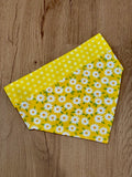 A yellow dog bandana with white daisies and polka dots pattern laid out flat on a wooden surface.
